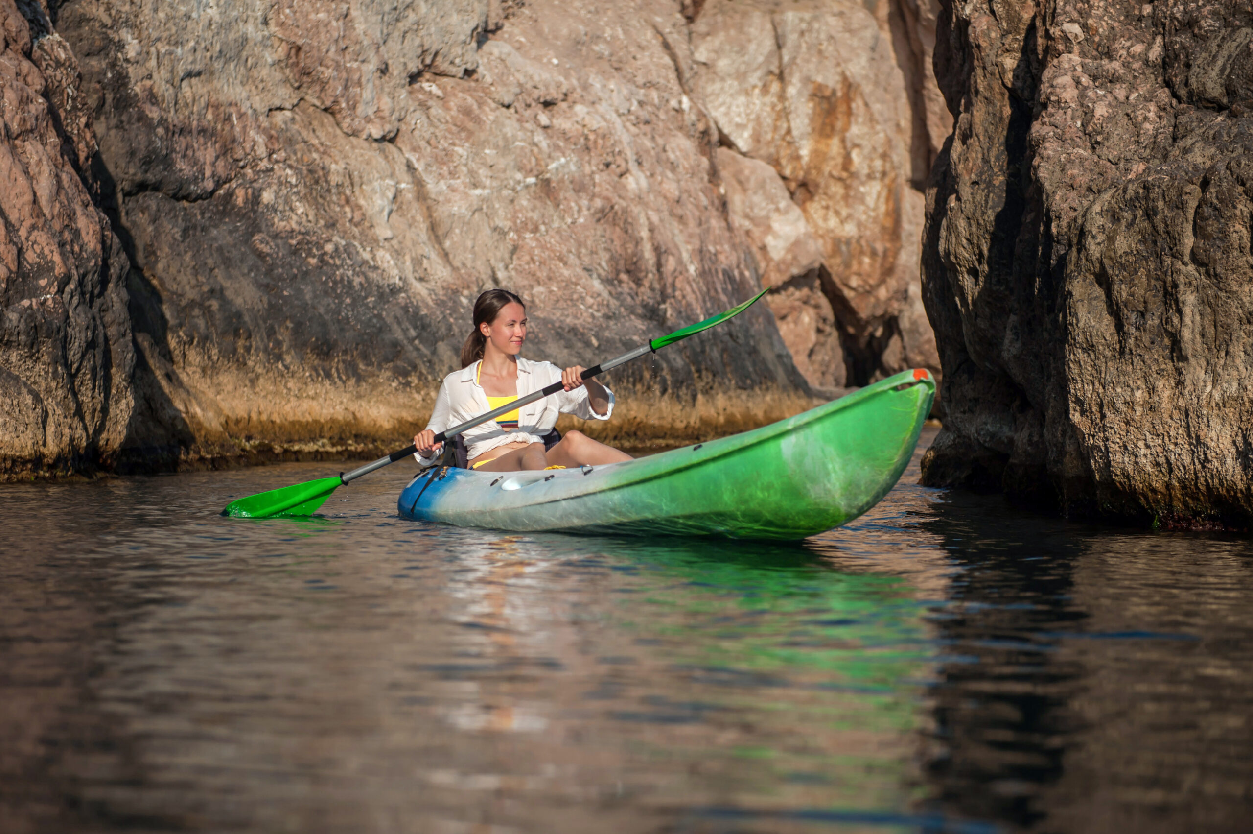 Girl swims in a kayak on the sea against the background of rocks near the shore
